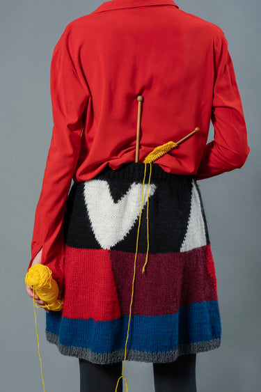 Back of woman wearing red top and wool skirt. The skirt has a colour block design made from blue, red, burgundy, black and white colours.